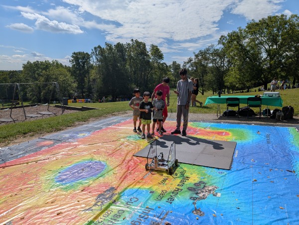 The chassis driving on a huge printed map outdoors while families watch