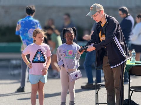An adult hands a controller to two young visitors